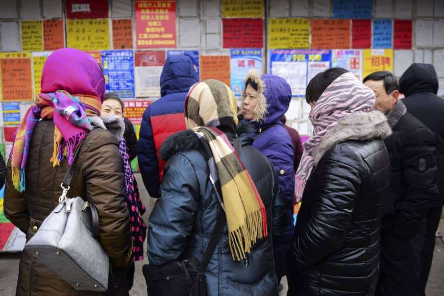 Women seeking work chat in front of a billboard displaying recruitment leaflets at a labor market in Qingdao, China, on Feb. 10. | Credit to the japan times